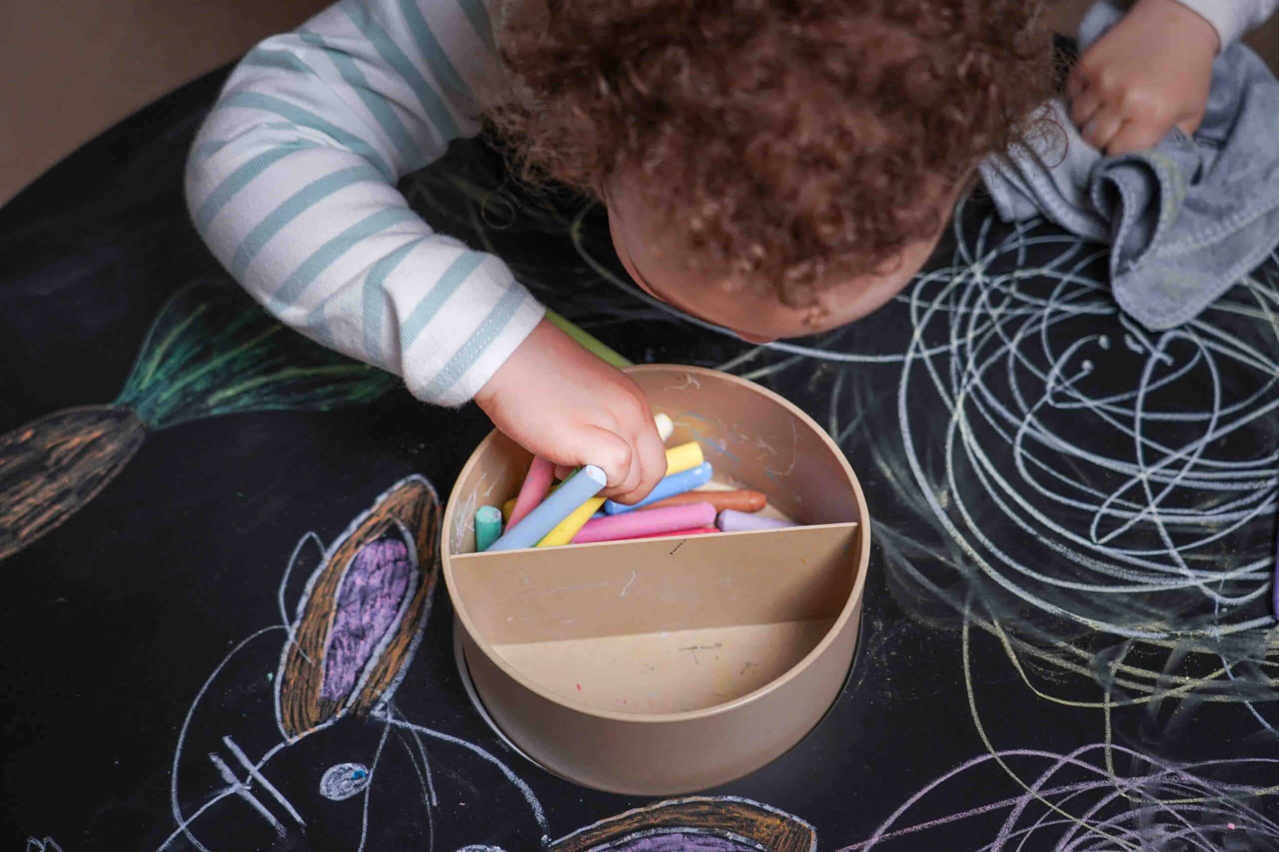 Enfant cherche une craie dans le pot central de la table de coloriage