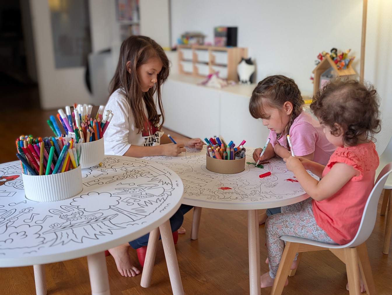 Trois enfants colorient à une table avec des feutres.
