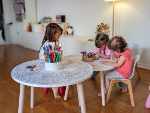 Trois enfants colorient autour de petites tables rondes