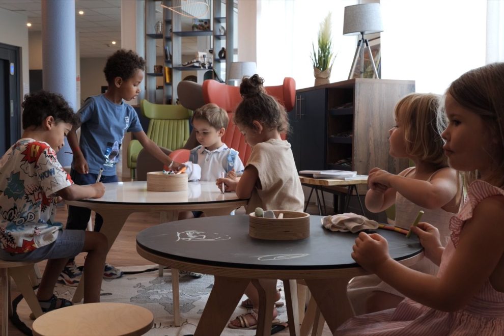 Enfants dessinant autour d'une table dans une salle.