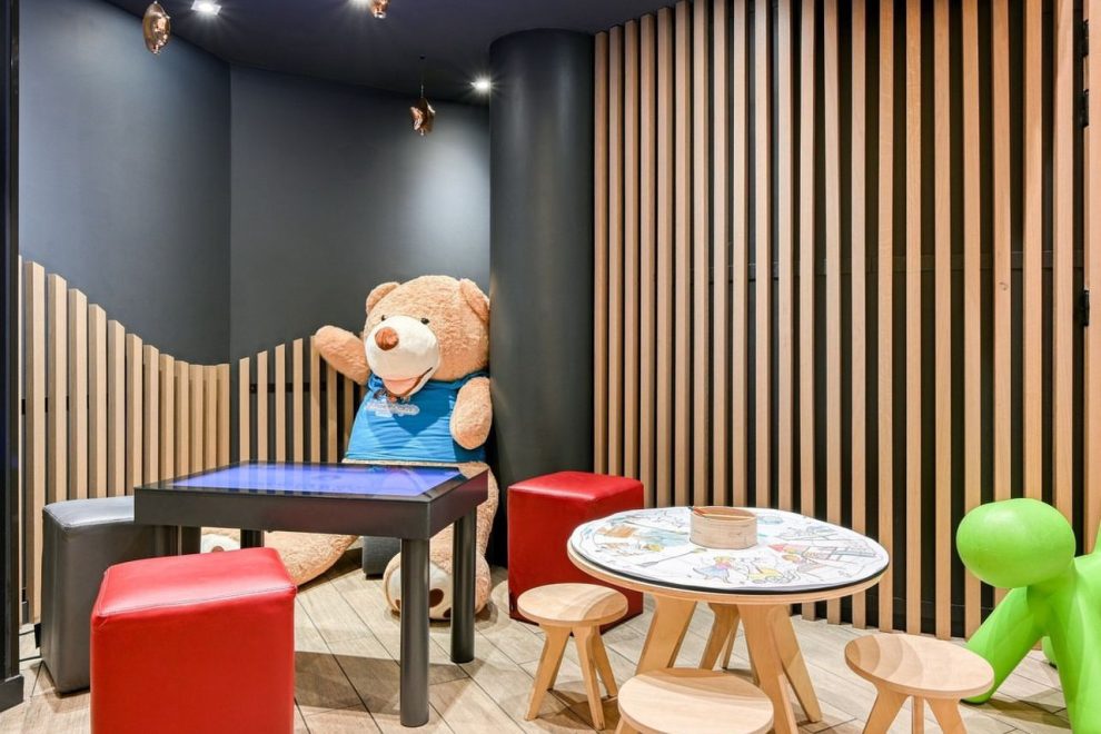 Coin enfant avec tables, chaises et ours en peluche.